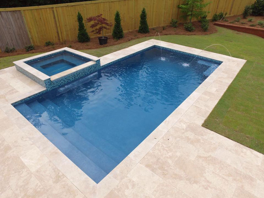 Mystic Pools custom gunite pool construction in Adel featuring a rectangular pool with arc fountain jets, raised square spa with mosaic tile and spillover, wide entry steps, and travertine paver decking with wood privacy fencing