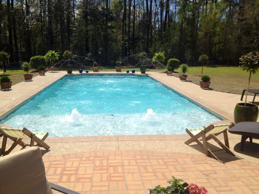 Mystic Pools custom saltwater gunite pool in Adel with multiple arc fountain jets, bubbler jets, brick paver patio, topiary plantings, decorative blue gazing balls, and lounge chairs surrounded by wooded landscaping