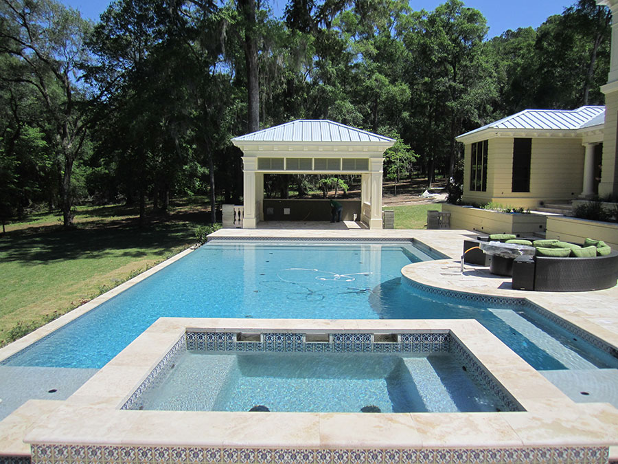 Mystic Pools custom rectangular gunite pool in Bainbridge with attached spa, decorative tile accents, travertine paver decking, circular lounging platform, and a classic pool house pavilion surrounded by Spanish moss-draped trees