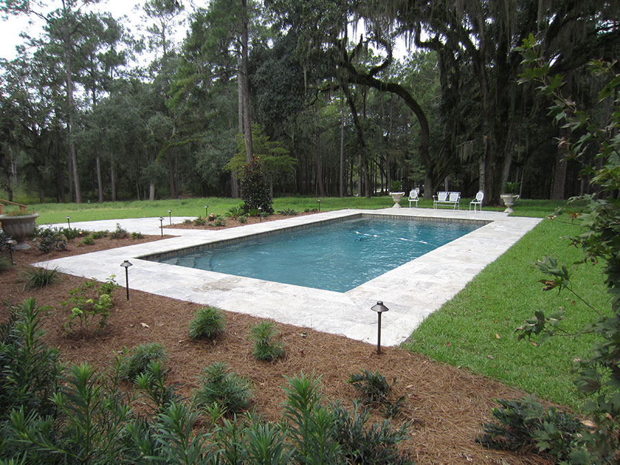 Mystic Pools custom saltwater gunite pool in Bainbridge with travertine paver decking, white outdoor seating, decorative urn planters, landscape path lighting, and mature Spanish moss-draped live oak trees