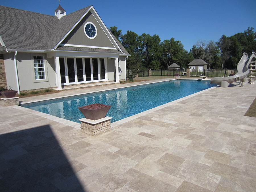 Mystic Pools custom saltwater gunite pool in Monticello with copper fire bowl pedestal, travertine paver decking, pool slide, and a pool house with cupola surrounded by black wrought iron fencing and trees