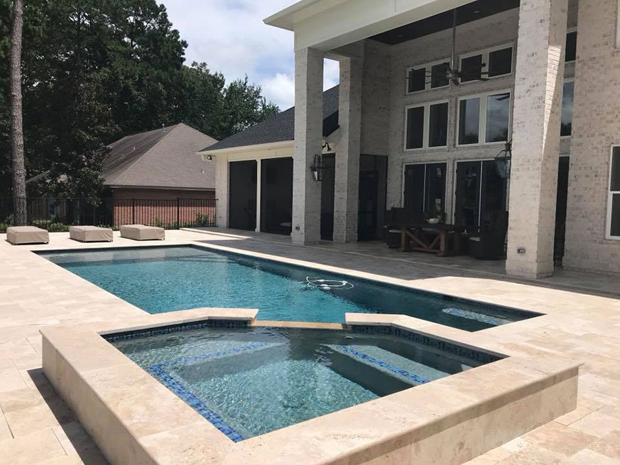 Mystic Pools custom saltwater gunite pool in Moultrie with raised square spa featuring blue mosaic tile, travertine paver decking, lounge ottomans, and a two-story stone estate home with covered outdoor living space