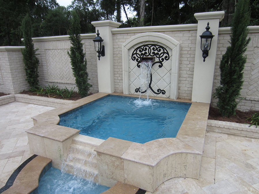 Mystic Pools custom gunite spa in Thomasville with ornate wrought iron wall fountain, herringbone brick accent wall, flanking columns with lanterns, Italian cypress trees, and travertine paver decking