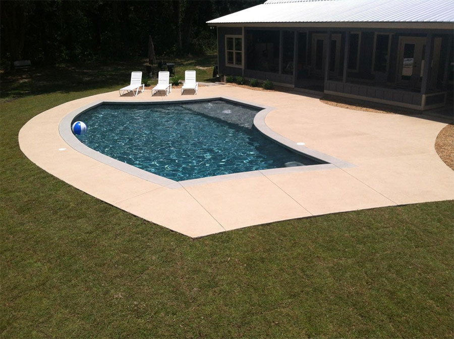 Aerial view of Mystic Pools remodeled freeform gunite pool in Tifton with dark finish, updated coping, wide concrete pool deck, white lounge chairs, and attached screened porch on a residential backyard