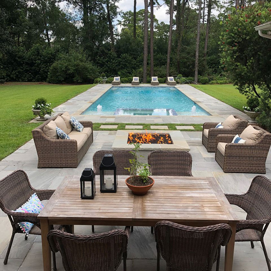 Mystic Pools custom rectangular gunite pool in Valdosta with attached spa, fountain jets, stone paver decking, fire pit seating area, and outdoor dining furniture surrounded by mature landscaping