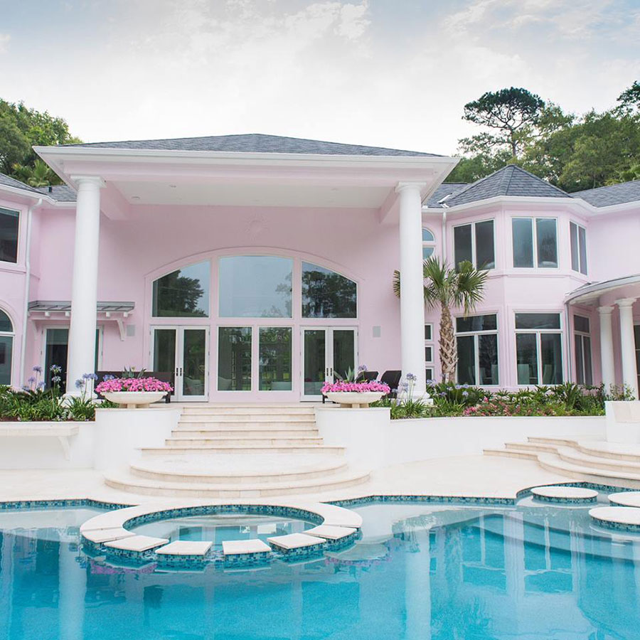 Mystic Pools custom luxury freeform gunite pool in Valdosta with submerged circular seating area, stepping stones, sweeping staircase entry, and large pink estate home with tropical landscaping