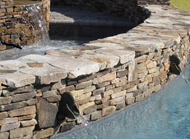 Mystic Pools custom pool featuring a curved natural fieldstone retaining wall with decorative bronze scupper spouts and sheer waterfall feature