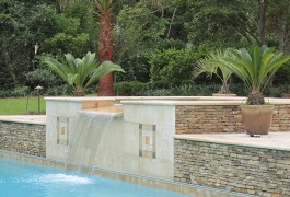Mystic Pools custom raised spa with sheer spillover waterfall, stacked stone retaining wall, and tropical palm and cycad landscaping