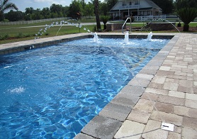 Mystic Pools custom rectangular gunite pool with in-pool fountain jets, brick paver decking, and residential backyard setting