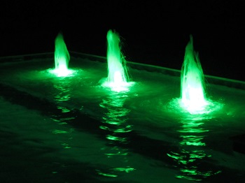 Three illuminated pool fountain jets with green LED underwater lighting photographed at night in a Mystic Pools custom gunite pool
